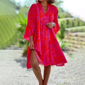 Robe d'été rouge à motifs floraux, manches longues, fendue, portée par une femme en extérieur. Mode féminine, tenue estivale élégante.
