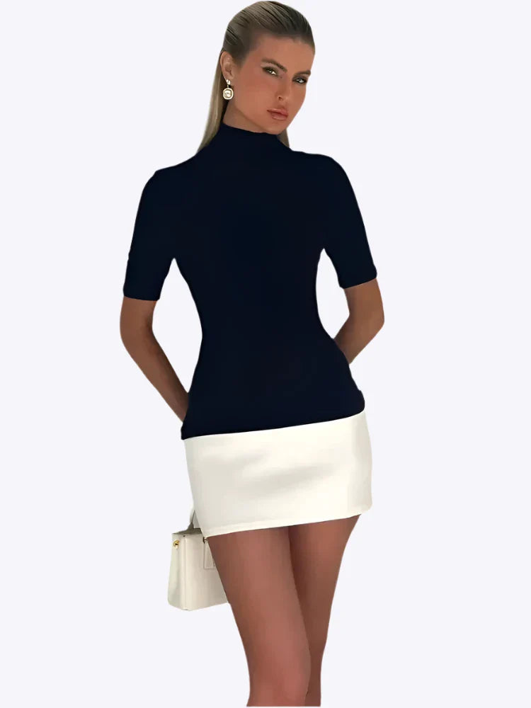 Femme portant un haut noir à manches courtes et une jupe blanche, posant avec un sac à main blanc. Mode élégante, tenue chic, style moderne.