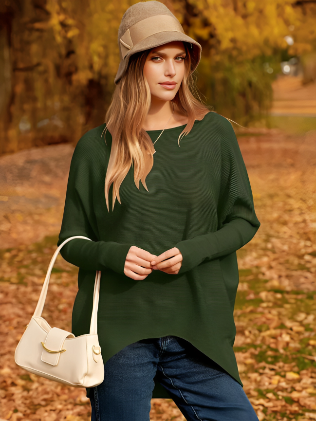 Femme en pull vert et chapeau beige, posant dans un parc automnal avec feuilles jaunes. Mode automne, style décontracté, sac à main blanc.