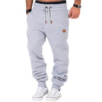 Homme portant un pantalon de jogging gris clair, cordons blancs, baskets blanches, montre noire; mode décontractée, style urbain tendance.