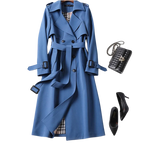 Manteau trench-coat bleu élégant avec ceinture, sac à main noir en cuir et escarpins noirs. Mode automne-hiver, style chic et sophistiqué.