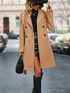 Femme élégante en manteau camel, jupe noire et bottes, tenant un sac à main noir, marchant en ville. Mode automne chic, style urbain sophistiqué.