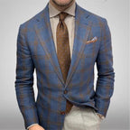 Homme en costume à carreaux bleu et marron, chemise rayée, cravate marron à motifs, pochette assortie, style élégant et moderne.