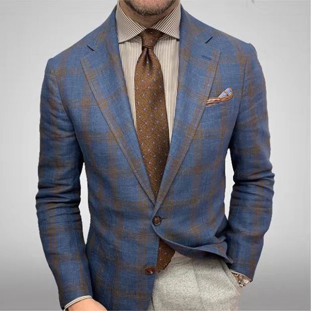 Homme en costume à carreaux bleu et marron, chemise rayée, cravate marron à motifs, pochette assortie, style élégant et moderne.