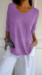 Femme portant un pull violet à manches longues et un pantalon blanc, avec un foulard rayé noir et blanc au poignet. Mode décontractée élégante.