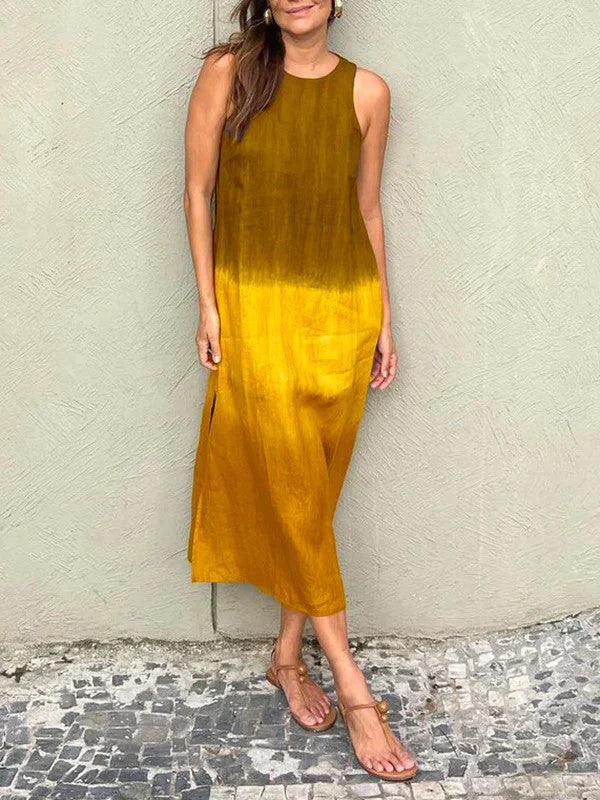 Robe longue dégradée jaune et marron, sans manches, portée par une femme debout sur un sol en mosaïque, sandales plates. Mode estivale élégante.