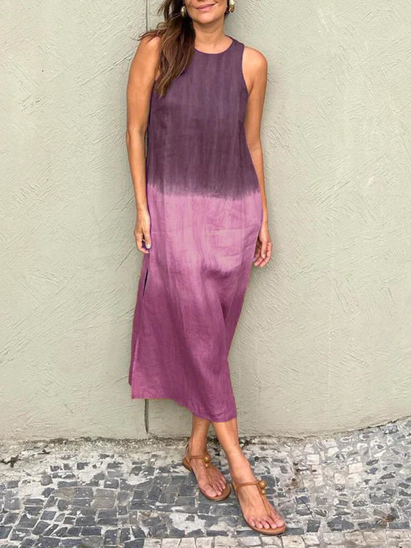 Robe longue dégradée violette portée par une femme, posant contre un mur texturé. Mode estivale, style décontracté, sandales plates.