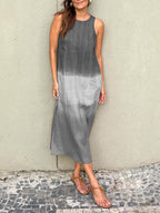 Robe longue dégradée gris, sans manches, portée par une femme sur fond de mur texturé. Mode estivale élégante, sandales marron.
