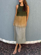 Robe longue dégradée vert kaki à beige, sans manches, portée par une femme. Style décontracté estival, sandales plates, mur gris en arrière-plan.