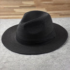 Chapeau Fedora noir en paille tressée sur fond gris, élégant et tendance, idéal pour la mode masculine et féminine. Accessoire chic et intemporel.