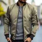Homme portant un blouson bomber kaki, manches longues, col noir, sur un t-shirt gris, en ville. Mode masculine, style urbain, tendance automne.