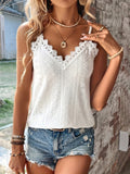 Femme portant un débardeur blanc en dentelle et un short en jean déchiré, accessoires dorés, posant près d'un mur en briques. Mode estivale décontractée.