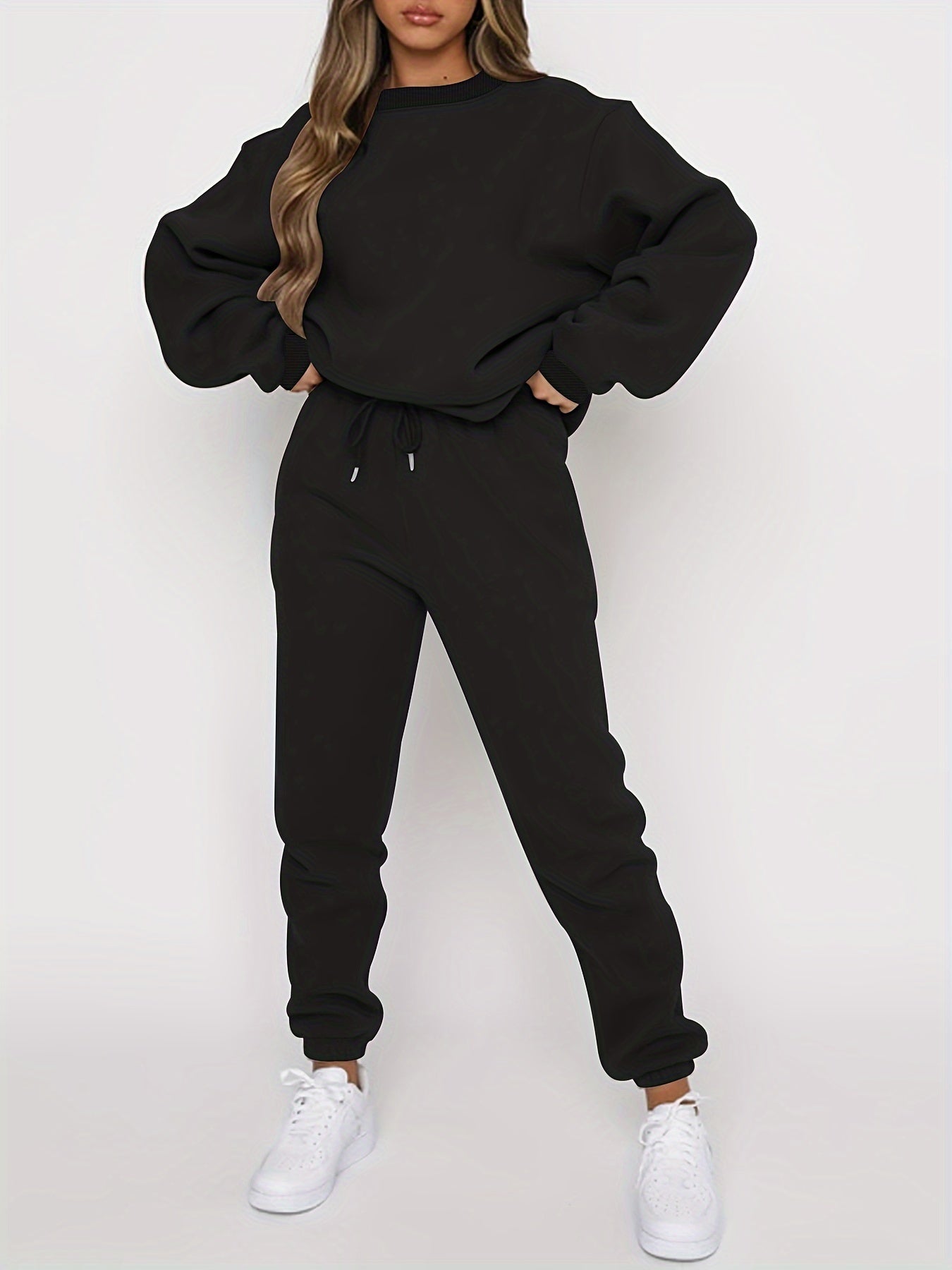 Femme en survêtement noir ample, baskets blanches, pose décontractée. Mode streetwear, tenue confortable, style moderne.