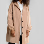 Personne portant un manteau beige à capuche, boutons noirs, sur une chemise blanche. Mode automne, style décontracté, vêtements tendance.