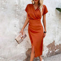 Robe orange élégante femme, manches courtes, coupe ajustée, fente latérale, accessoirisée d'un sac à main beige, mode tendance.