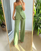 Femme en combinaison verte élégante, posant devant un miroir, tenue chic et moderne, mode féminine tendance, intérieur lumineux avec plantes.