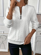 Femme portant un pull blanc texturé à fermeture éclair, posant dans un intérieur moderne. Mode automne-hiver, style élégant et décontracté.