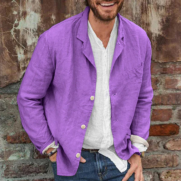 Homme souriant portant une veste en lin violet sur une chemise blanche, posant devant un mur en briques. Mode décontractée, style estival.