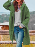 Femme portant un manteau vert en laine, écharpe colorée, pull gris et jean, posant en extérieur. Mode automne-hiver, style décontracté.