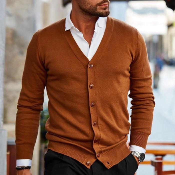 Homme portant un cardigan marron élégant sur une chemise blanche, style mode masculine chic, rue urbaine en arrière-plan.