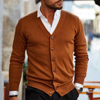 Homme portant un cardigan marron élégant sur une chemise blanche, style mode masculine chic, rue urbaine en arrière-plan.