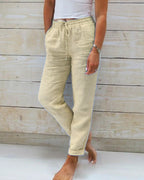 Pantalon en lin beige pour femme, taille élastique avec cordon, poches latérales, style décontracté, fond en bois clair.
