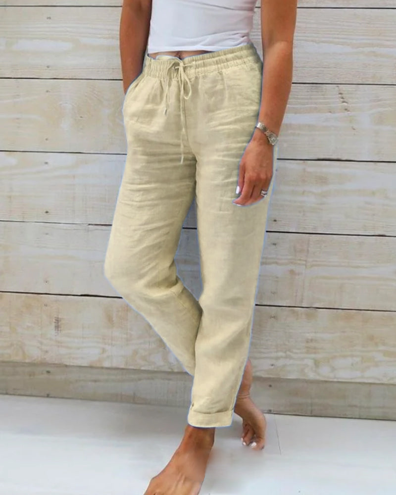 Pantalon en lin beige pour femme, taille élastique avec cordon, poches latérales, style décontracté, fond en bois clair.