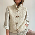 Gilet en laine tricoté à la main, couleur crème, avec boutons en bois, porté sur une chemise beige. Mode automne-hiver, style décontracté et élégant.