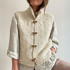 Gilet en laine tricoté à la main, couleur crème, avec boutons en bois, porté sur une chemise beige. Mode automne-hiver, style décontracté et élégant.