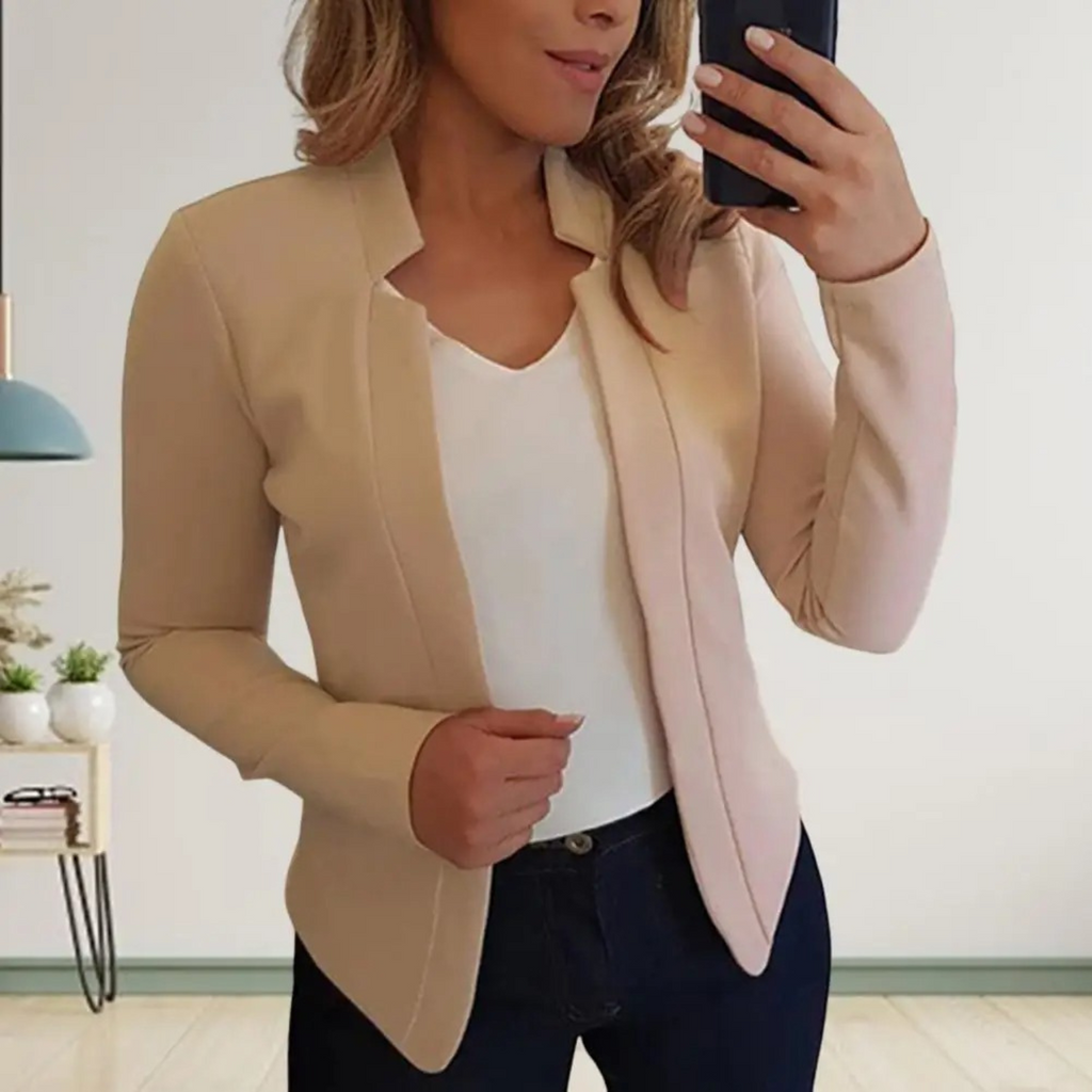 Femme en blazer beige, chemise blanche et jean, prenant un selfie dans un miroir. Mode élégante, tenue décontractée chic, intérieur moderne.