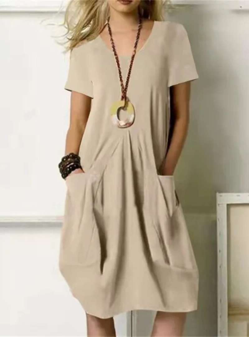 Robe beige ample avec poches, collier pendentif rond, femme blonde. Mode décontractée, style estival, tenue élégante et confortable.