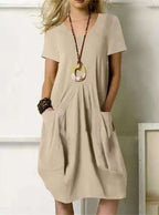 Robe beige ample avec poches, collier pendentif rond, femme blonde. Mode décontractée, style estival, tenue élégante et confortable.