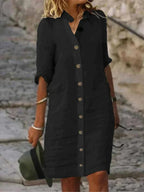 Robe chemise noire à manches longues, boutonnée, portée par une femme blonde sur un escalier en pierre. Mode élégante, tenue décontractée.