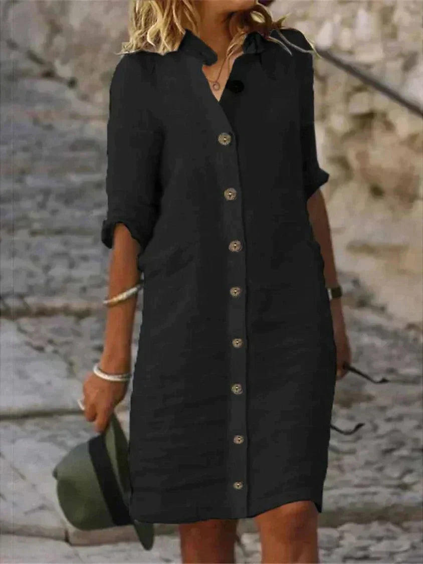 Robe chemise noire à manches longues, boutonnée, portée par une femme blonde sur un escalier en pierre. Mode élégante, tenue décontractée.