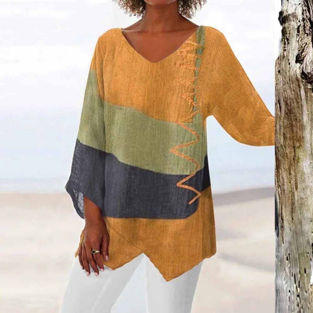 Femme portant un haut ample coloré à manches longues, motifs géométriques vert, orange et noir, sur fond de plage. Mode décontractée, style estival.