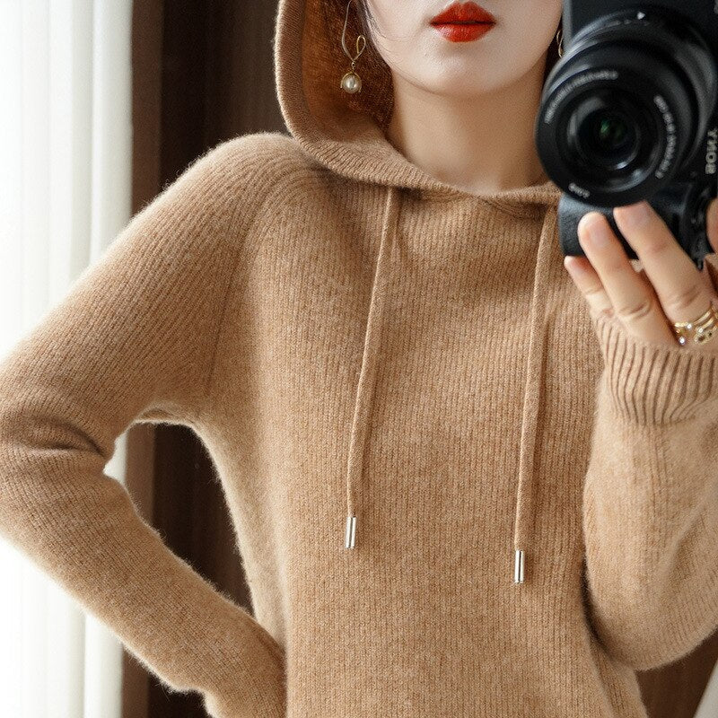 Femme en pull à capuche beige en laine, tenant un appareil photo. Mode automne-hiver, style décontracté, photographie lifestyle.