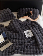 Femme dormant sous une couverture en fausse fourrure grise avec oreillers assortis, magazine et ordinateur portable sur le lit. Confort et détente.