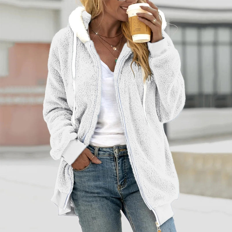 Femme portant un manteau en fausse fourrure blanc, tenant un café à emporter. Mode décontractée, jeans, style automne-hiver, confort et élégance.