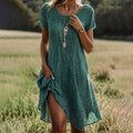 Robe d'été verte à pois blancs portée par une femme dans un champ, accessoirisée avec des colliers et une montre. Mode féminine, style champêtre.