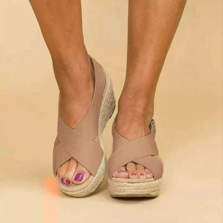 Sandales compensées beiges avec semelle en corde, portées par une personne sur fond beige. Chaussures d'été élégantes et confortables.