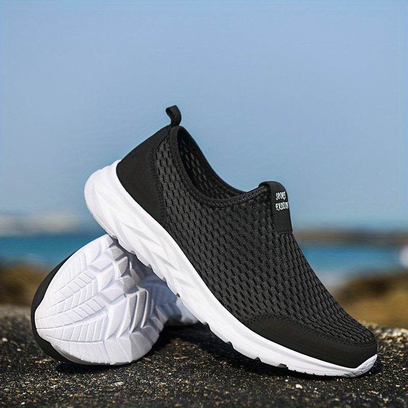 Chaussures de sport noires en maille respirante avec semelles blanches, posées sur un sol rocheux, ciel bleu en arrière-plan.
