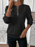 Femme portant un pull noir texturé avec fermeture éclair, posant dans un intérieur moderne. Mode automne, style élégant, tenue décontractée chic.