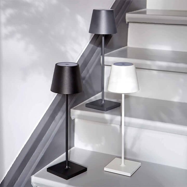 Trois lampes de table modernes en métal noir, gris et blanc sur des marches d'escalier, design minimaliste, éclairage intérieur élégant.
