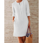 Robe blanche en lin pour femme avec manches longues, boutons sur le devant, poches latérales, accompagnée d'un sac en osier. Mode estivale élégante.