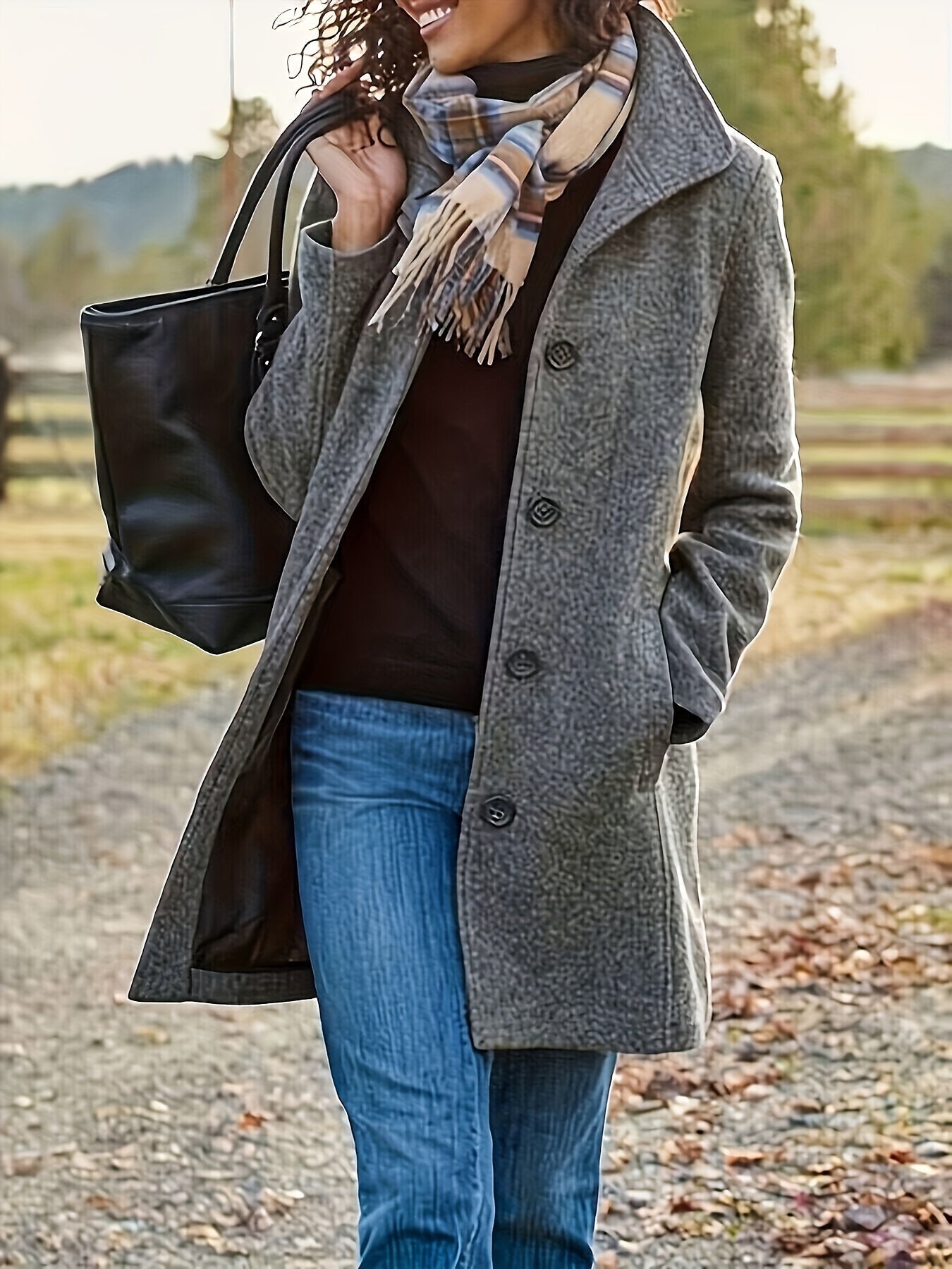 Femme portant un manteau gris élégant, écharpe à carreaux, sac noir, marchant sur un chemin automnal. Mode automne, style décontracté chic.