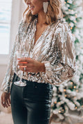 Femme portant un haut à paillettes argentées et un pantalon noir, tenant un verre de vin, devant un sapin de Noël décoré. Mode festive élégante.