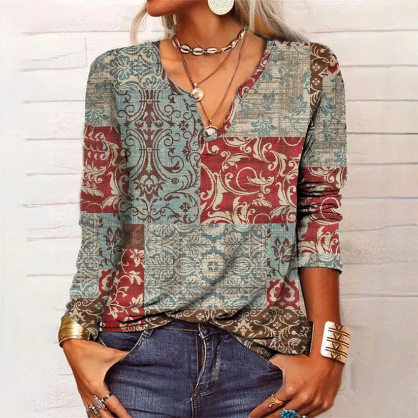 Femme portant un pull patchwork bohème à motifs floraux rouges et bleus, col en V, manches longues, accessoires dorés, style décontracté chic.