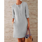 Robe en lin gris clair à manches longues, boutons sur le devant, poches latérales, tenue décontractée pour femme, fond en bois clair.
