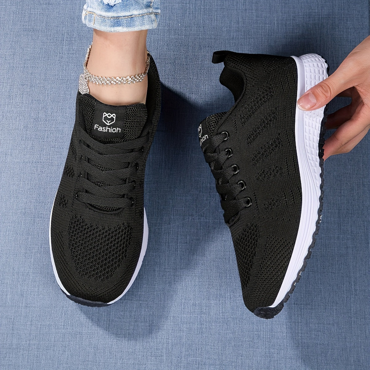Chaussures de sport noires pour femme sur fond bleu, avec semelle blanche texturée. Design moderne et confortable, parfait pour la mode et le fitness.