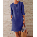 Robe en lin bleu avec manches longues retroussées, poches avant, portée par une femme tenant un sac en osier. Mode féminine élégante et décontractée.